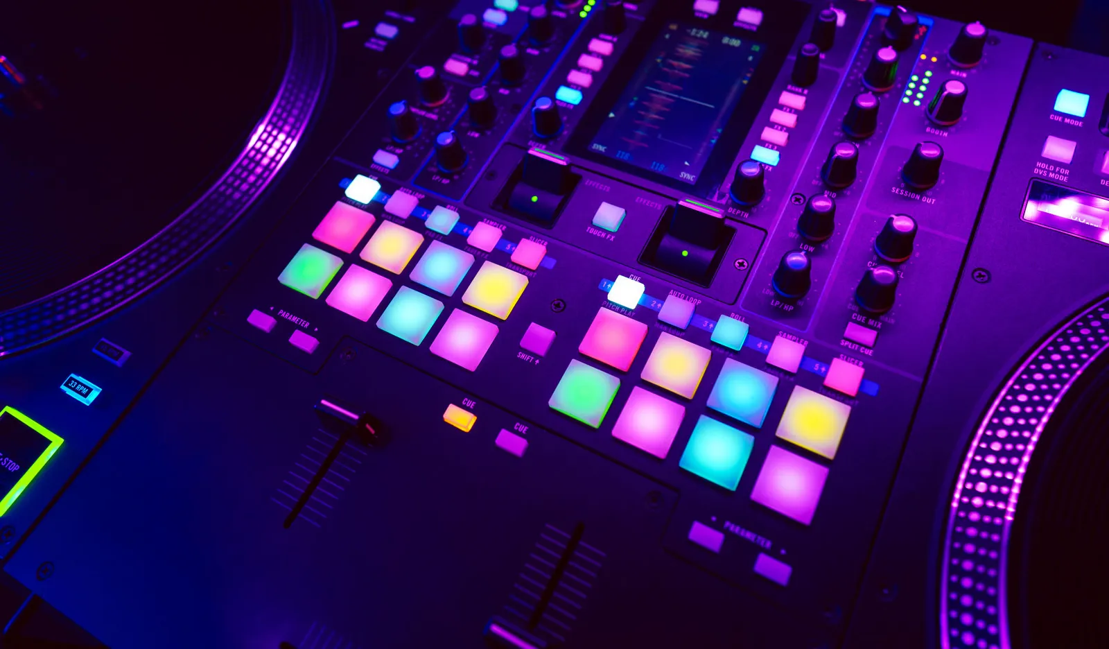 Nahaufnahme eines beleuchteten DJ-Mixpults mit bunten Performance-Pads in Pink, Blau und Gelb
