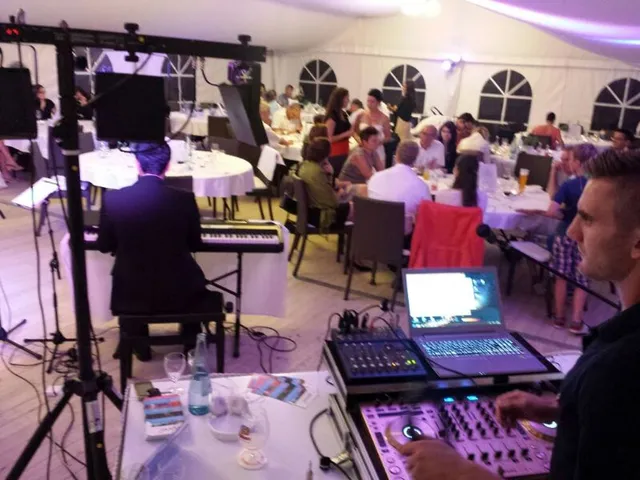 DJ und Live-Keyboarder spielen in einem festlich gedeckten Hochzeitszelt vor sitzenden Gästen